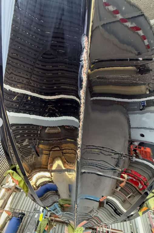 A highly reflective black Boat Hull showing distorted reflections of a garage or workshop environment.