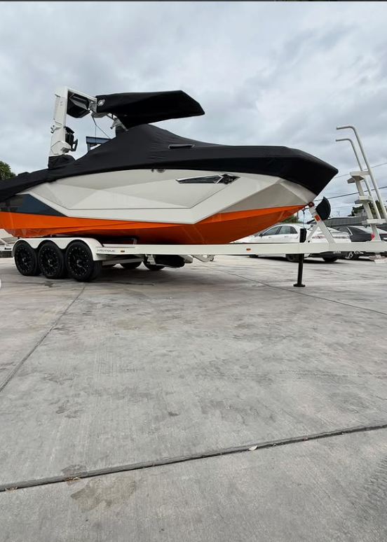 A large motorboat on a trailer parked on a concrete lot with overcast sky in the background.