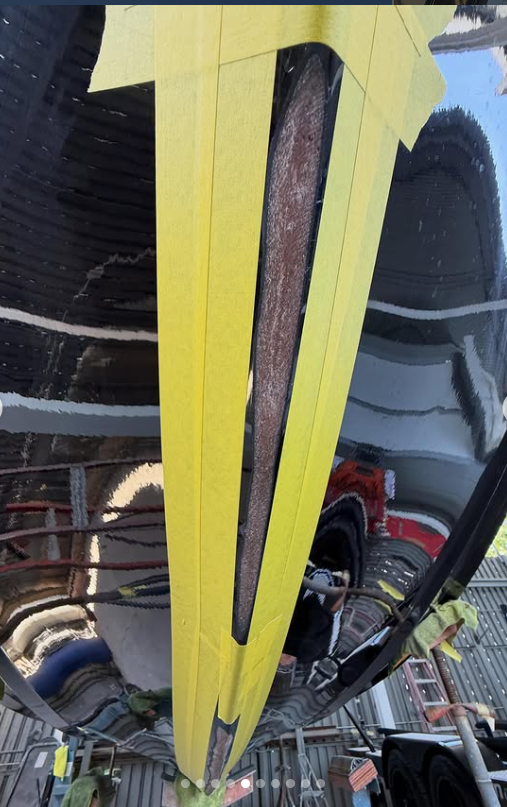 Close-up of a black Boat Hull with yellow tape applied in a straight line, covering a strip of rust.