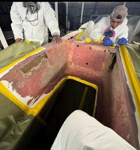 Two workers in protective gear doing a fiberglass repair at the interior of a boat hull undergoing restoration or repair at sergio's boat spa boat repair shop.