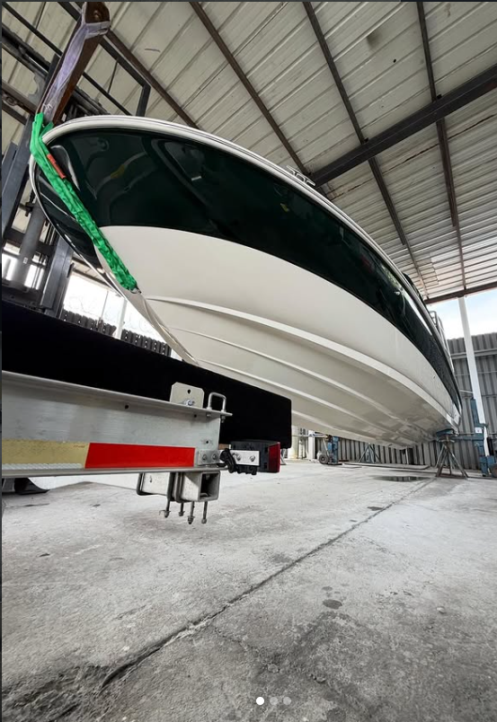 A large white and green boat stored inside a warehouse, hanging slightly above the ground supported by a trailer or lift.