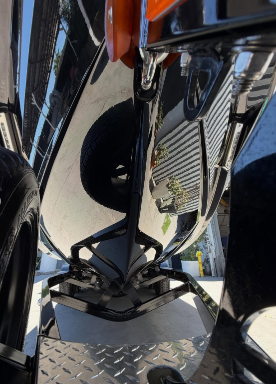 Close-up of a black Boat Hull with a reflective surface showing a striped wall and some plants, captured from above.