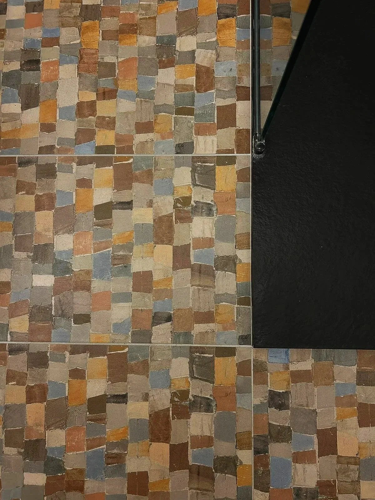 Un mur en mosaïque de petits carreaux de différentes couleurs, avec une partie noire en pierre polie à droite.