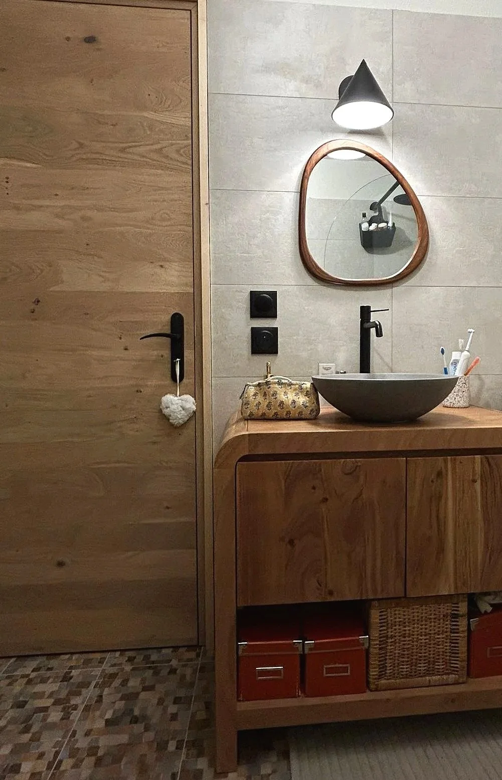 Un lavabo rond en pierre sur une console en bois dans une salle de bain avec un miroir, un éclairage noir, et des accessoires de salle de bain.