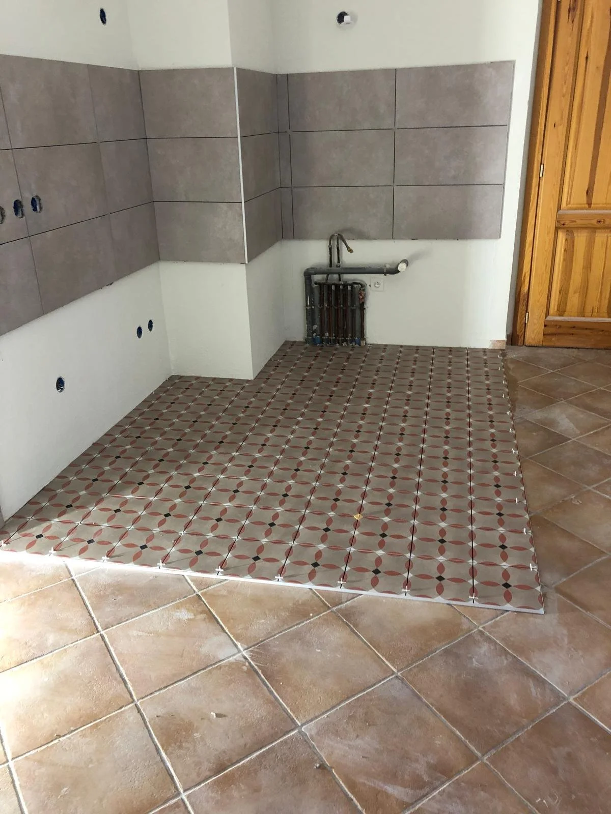 Rénovation de cuisine avec carrelage au sol et gros plan sur la zone de travail avec plomberie et mur partiellement carrelé