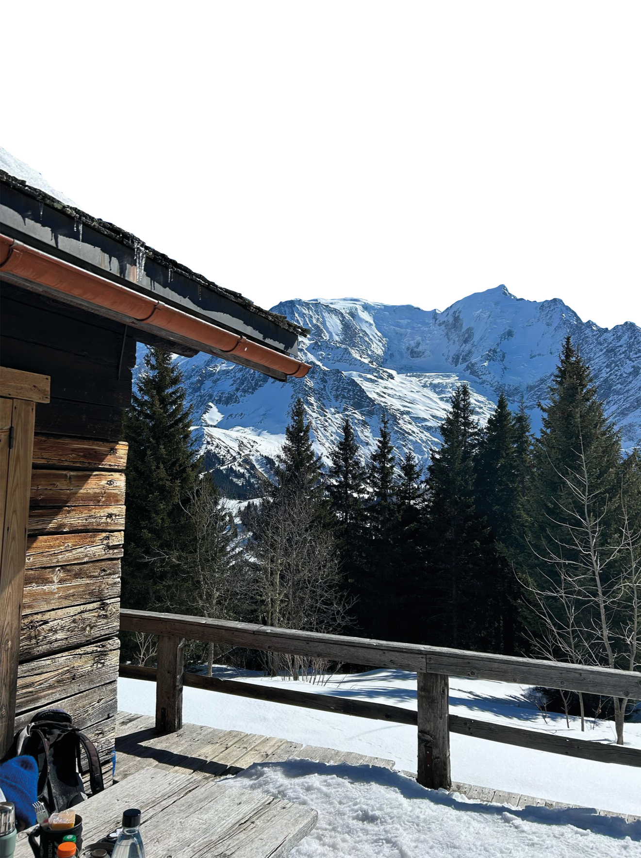 Une cabane en bois dans un paysage montagneux enneigé, avec des sapins et des montagnes couvertes de neige en arrière-plan, dans un cadre alpin en hiver.