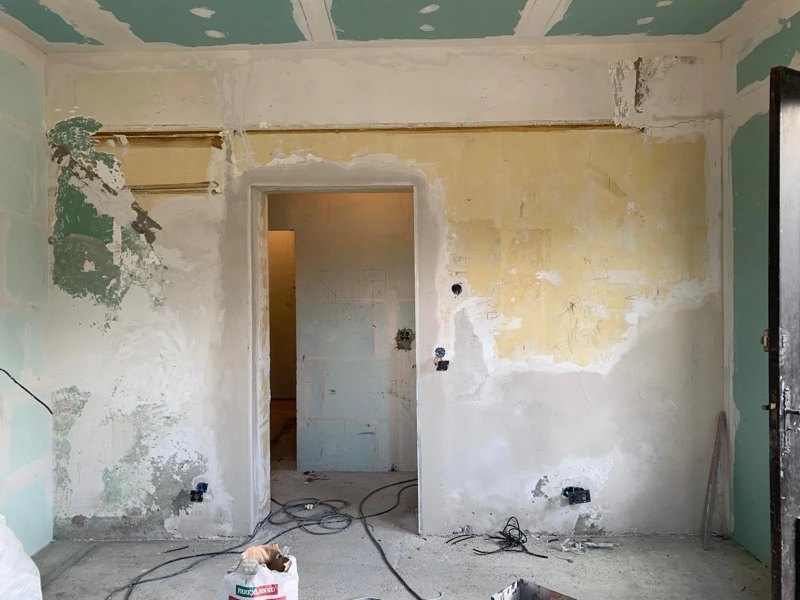 Une pièce en cours de rénovation avec des murs en plâtre partiellement enduits, câbles électriques au sol, et un espace de porte sans porte encore installé.