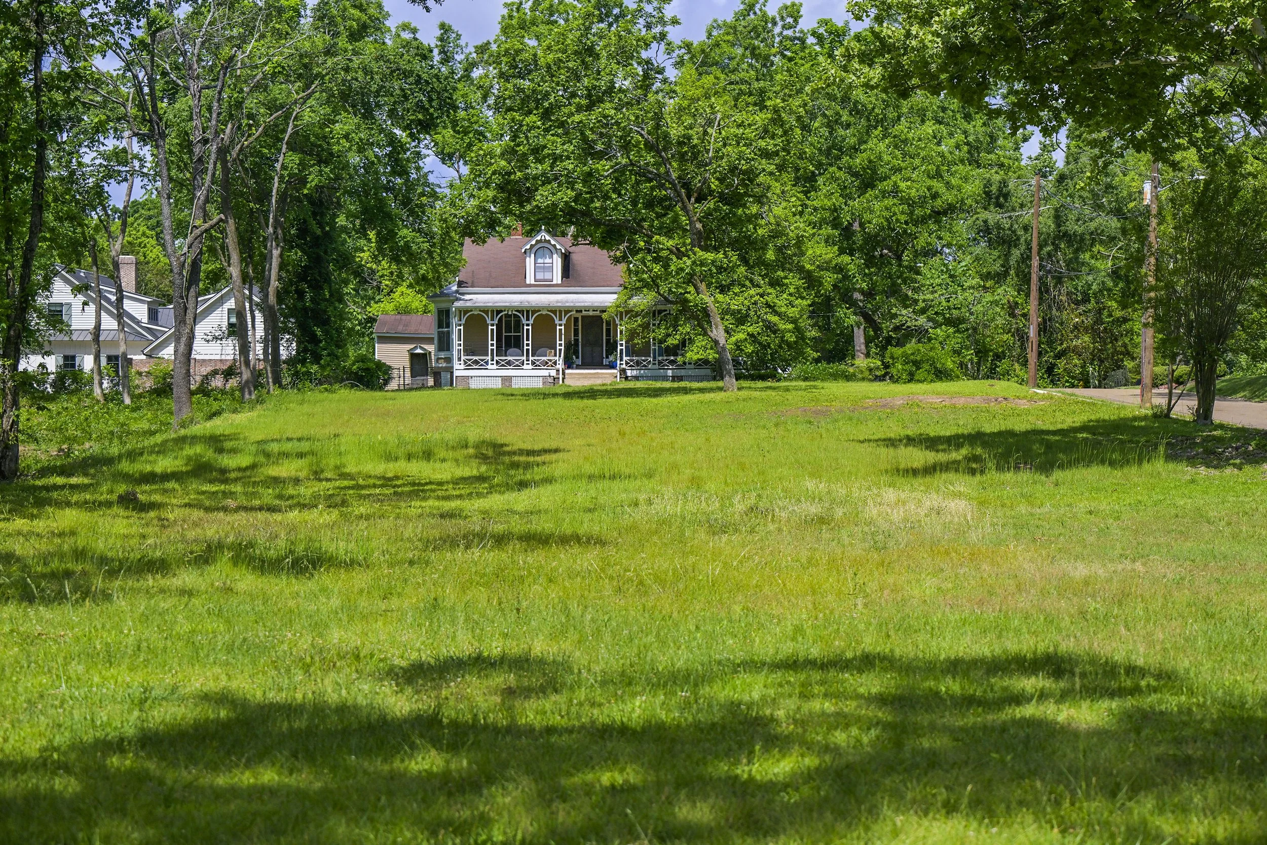 A house with a porch surrounded by large trees and a lawn, with power lines visible to the right.