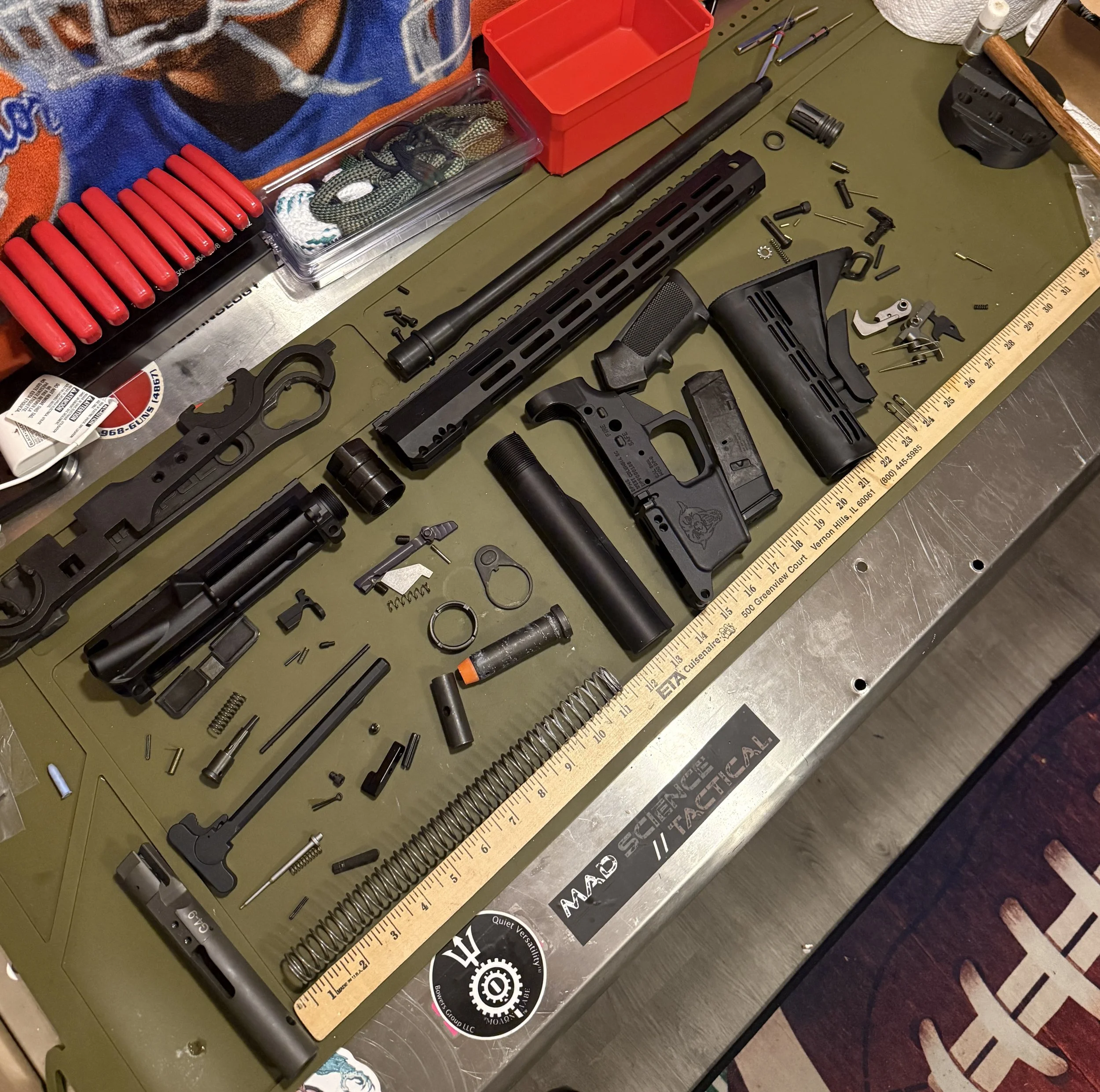 Disassembled firearm parts laid out on a green work surface with a ruler, tools, and accessories nearby.