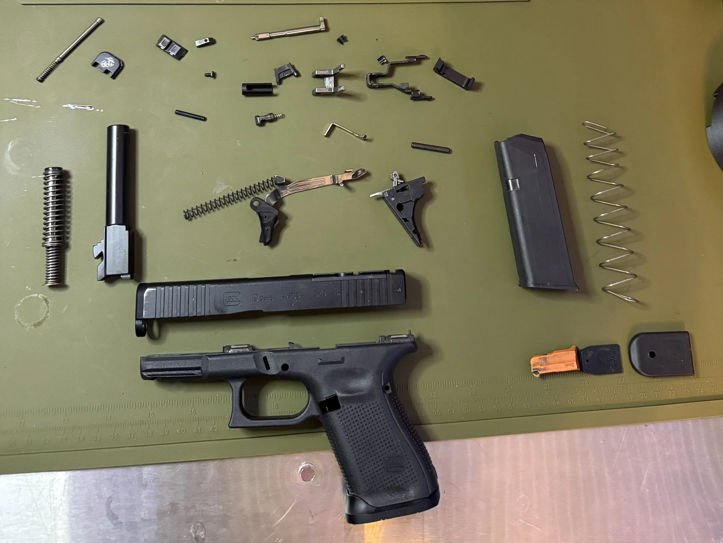 Disassembled semi-automatic handgun parts laid out on a green cutting mat, including a slide, barrel, spring, magazine, and various small components.