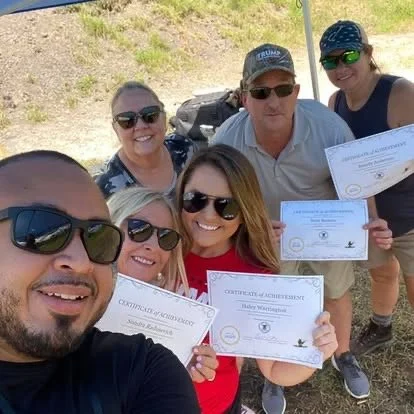 Six people outdoors smiling, holding certificates of achievement.