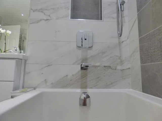 A bathroom with a bathtub, tiled walls, a wall-mounted faucet, a showerhead, and a small window.