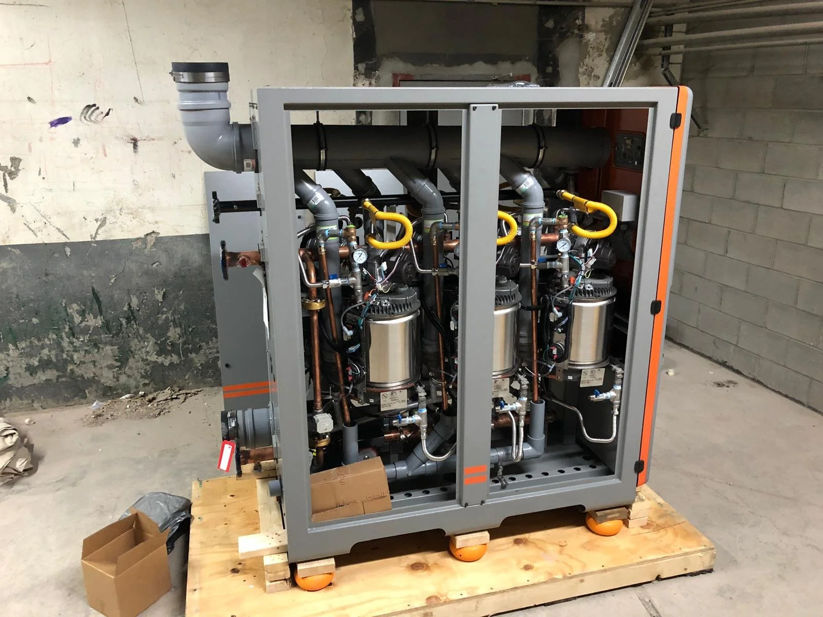 Industrial machine with pipes, gauges, and metallic components on a wooden pallet in a construction area.