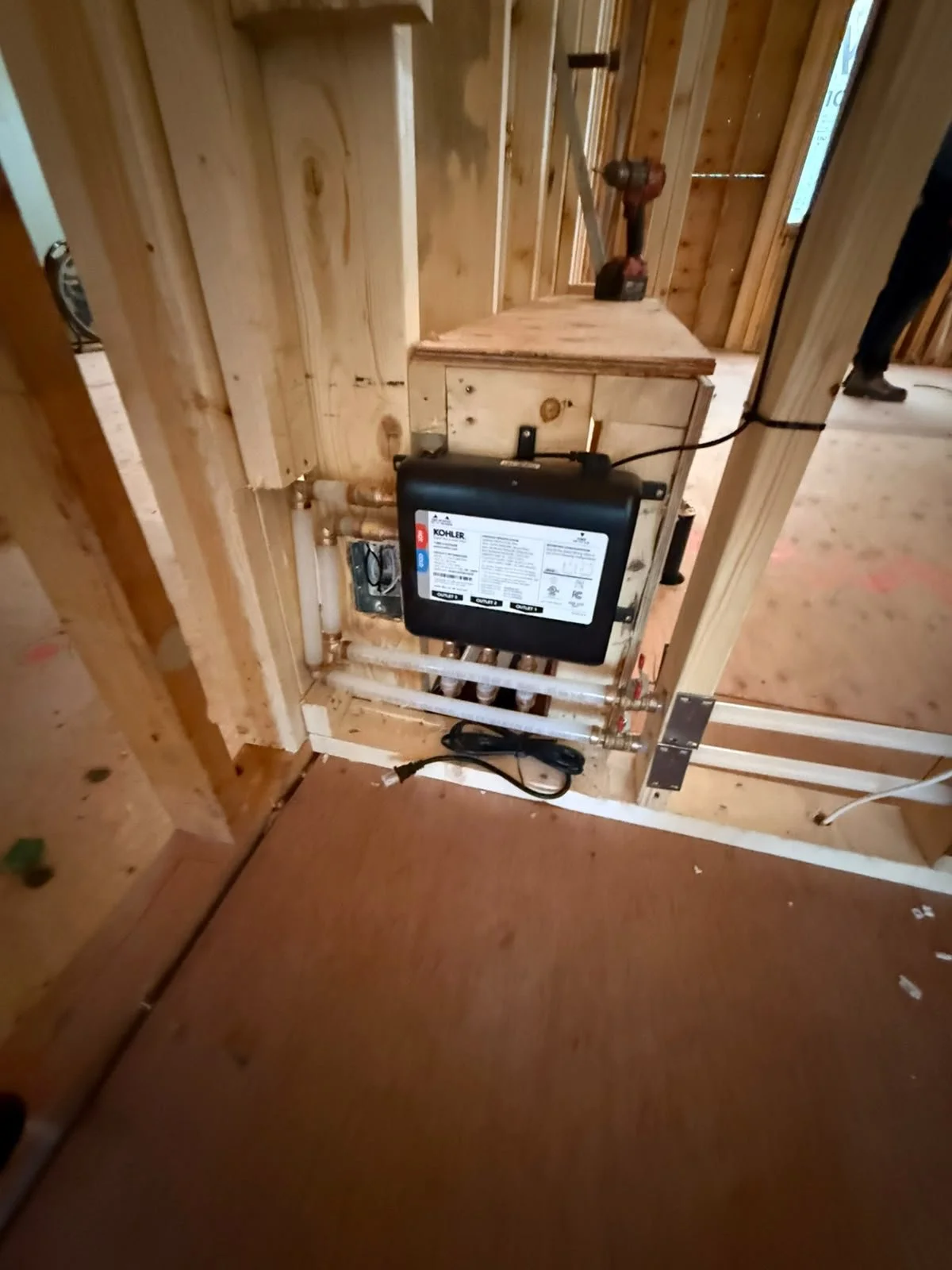Construction site with plumbing and a Kohler water heater or pump installed in a wooden frame wall.