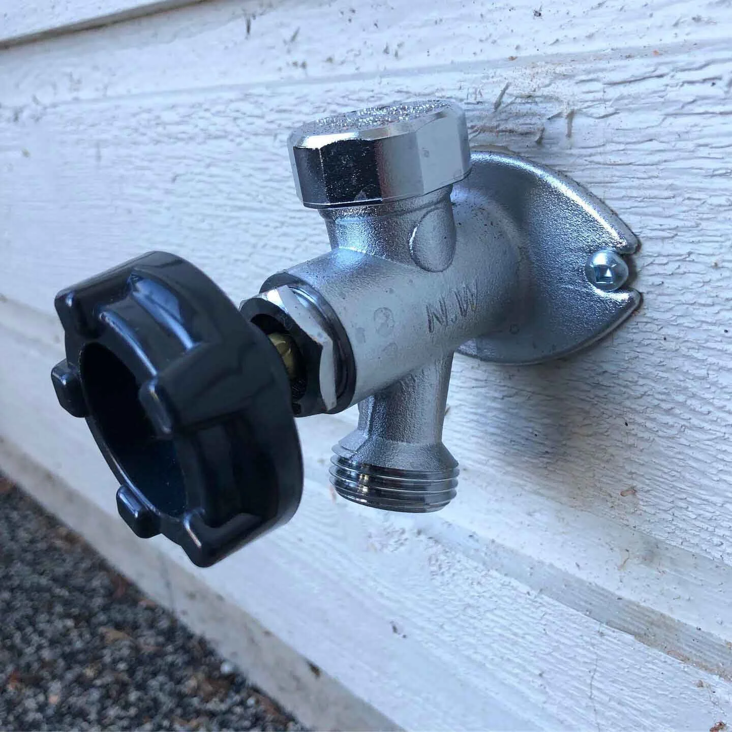 Exterior water spigot attached to a white house wall, with a black handle for controlling water flow.