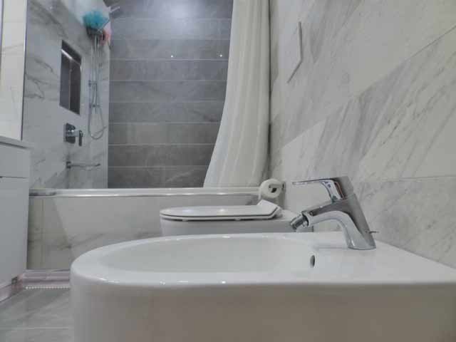 Bathroom scene with a white sink, a toilet, and a shower area with a curtain in the background, featuring modern gray tiled walls.