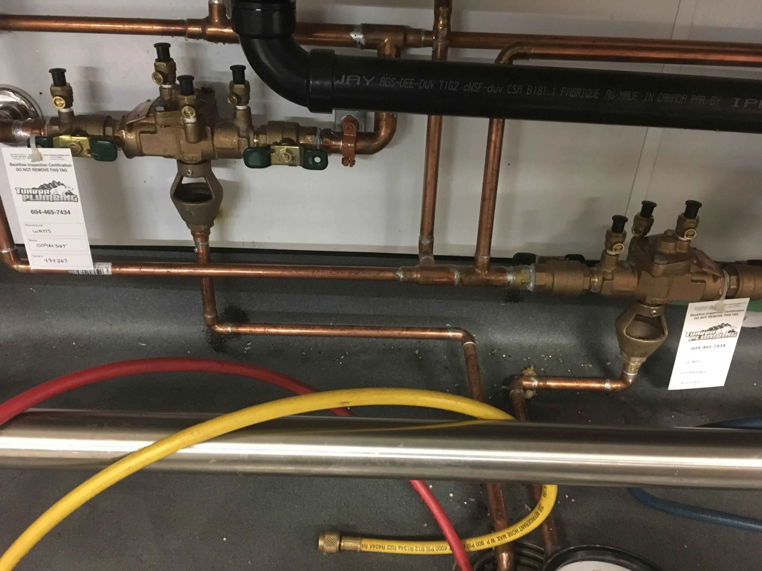 A plumbing system with copper pipes, brass valves, black pipe, and colored hoses. There are labels and tags attached to some components for inspection and identification.
