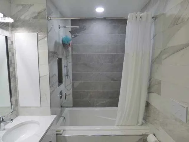 Bathroom with a shower, bathtub, white curtain, sink, and tiled walls.