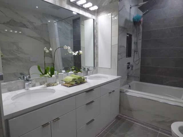 Modern bathroom with double vanity sinks, large mirror, orchids, folded towels, bathtub, and shower head with blue shower puff.