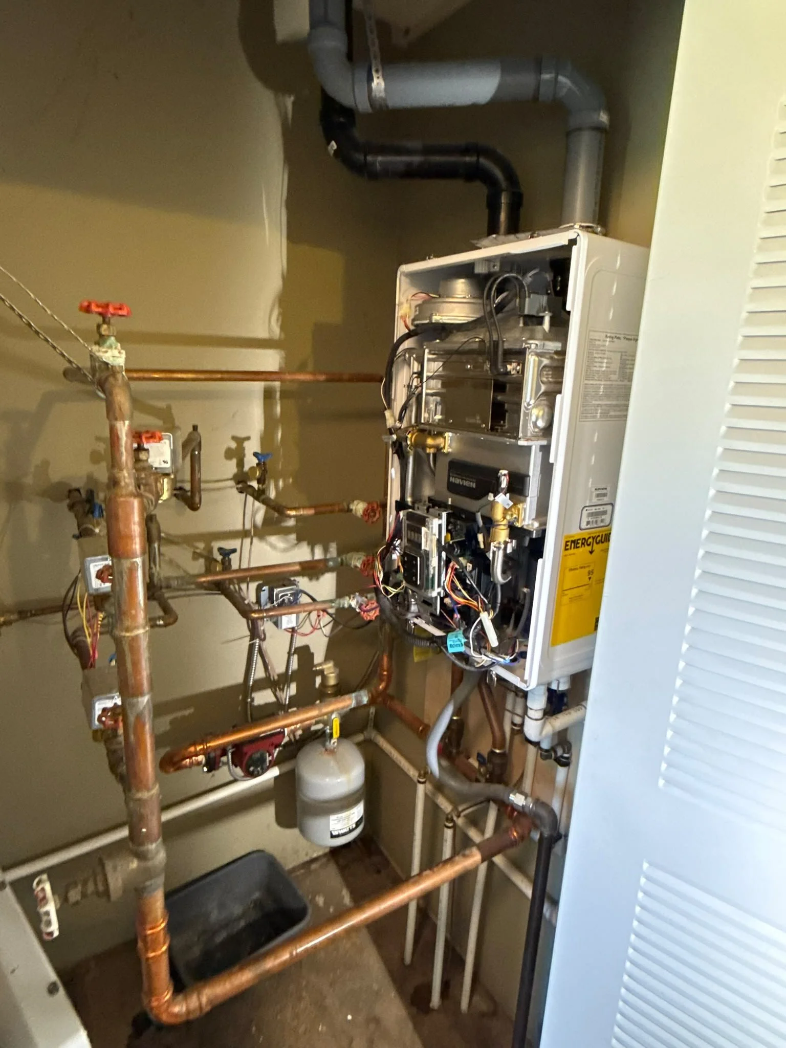 Open furnace with exposed heating components, copper pipes, and a pressure tank in a utility closet.