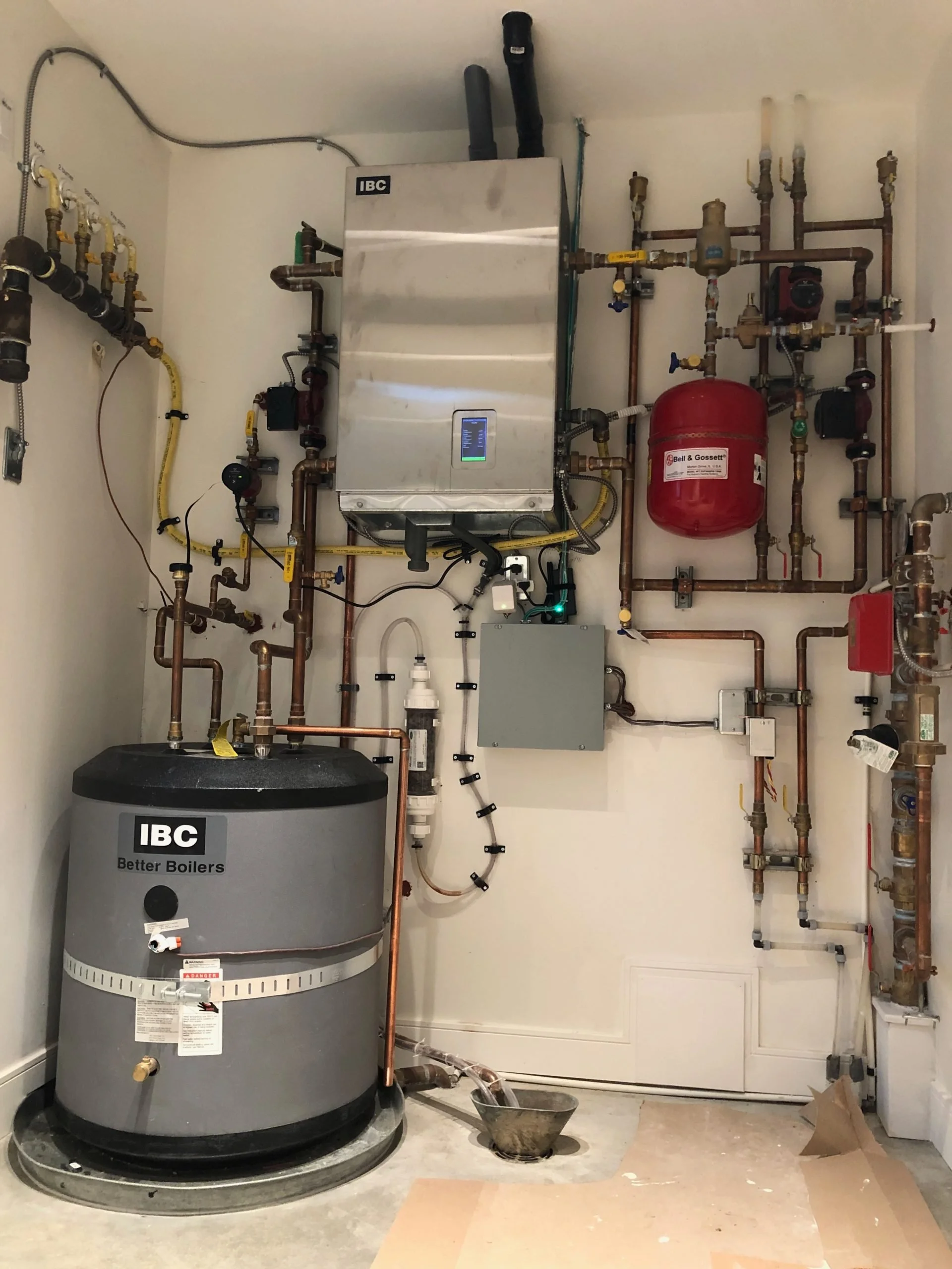 A utility room with a boiler, a pressure tank, and various pipes and valves.