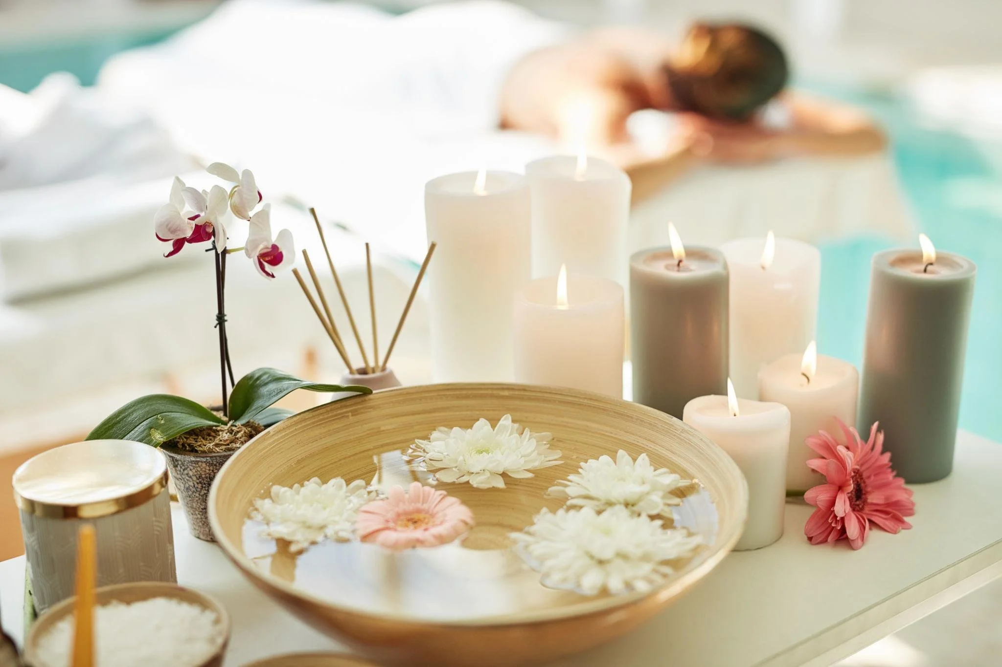 A table decorated with white and pink flowers in bowls, white candles, and orchids in small pots, creating a serene and elegant ambiance.