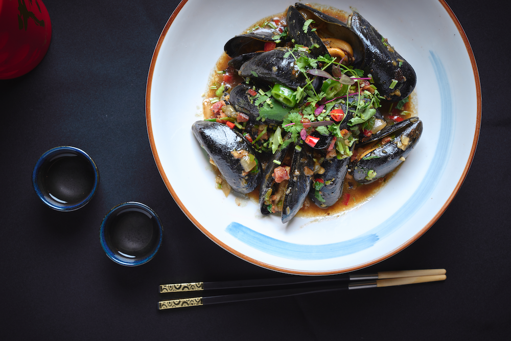 A plate of steamed mussels topped with chopped green onions, cilantro, and red peppers.