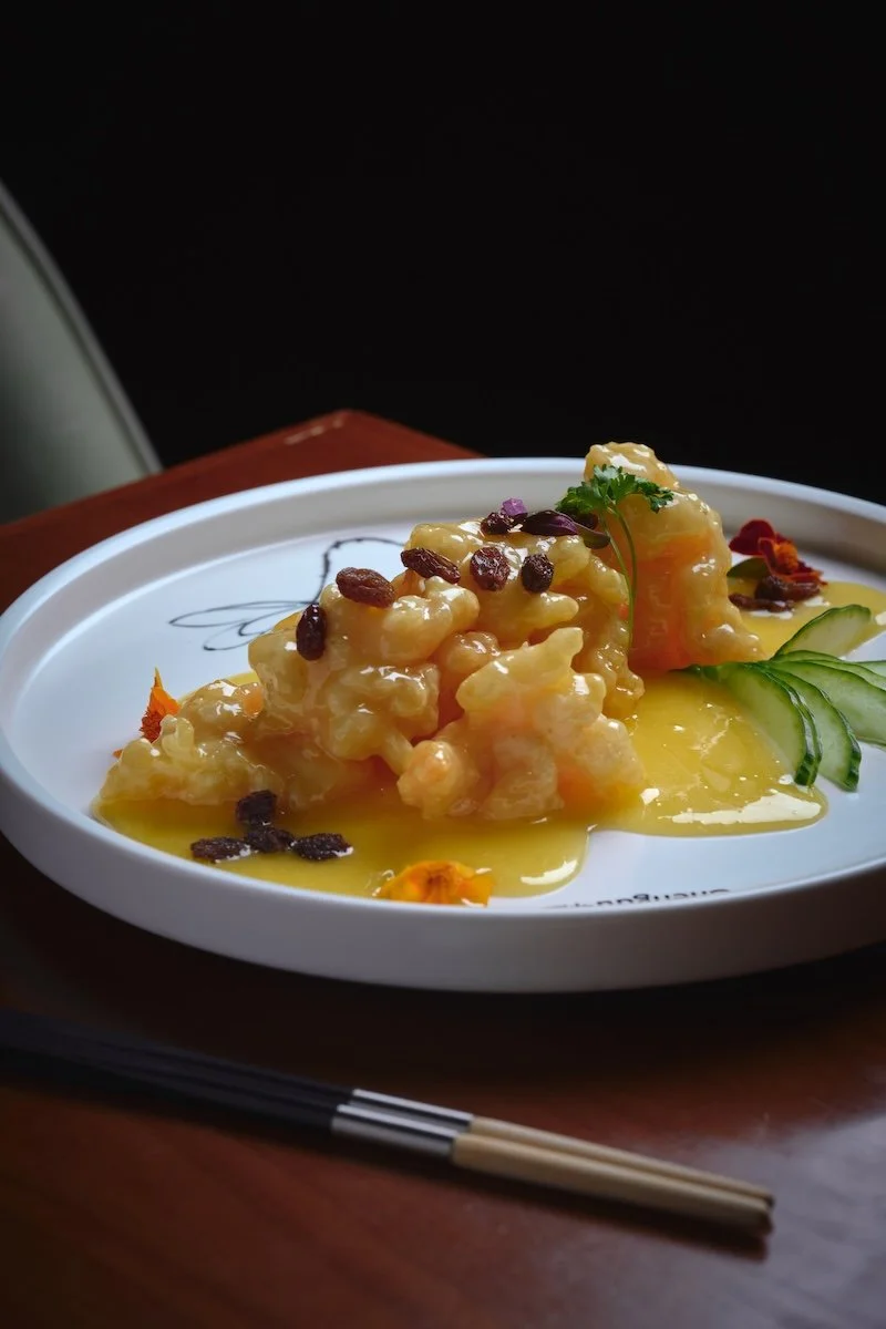 Shrimp garnished with dried berries and cilantro, served with cucumber slices and a orange liquor sauce on a white plate
