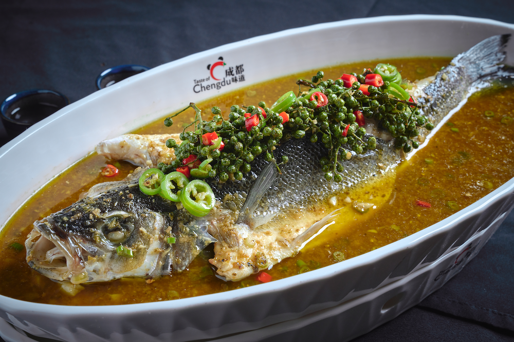 Whole steamed fish garnished with chopped red and green chili peppers, served with a spicy broth.