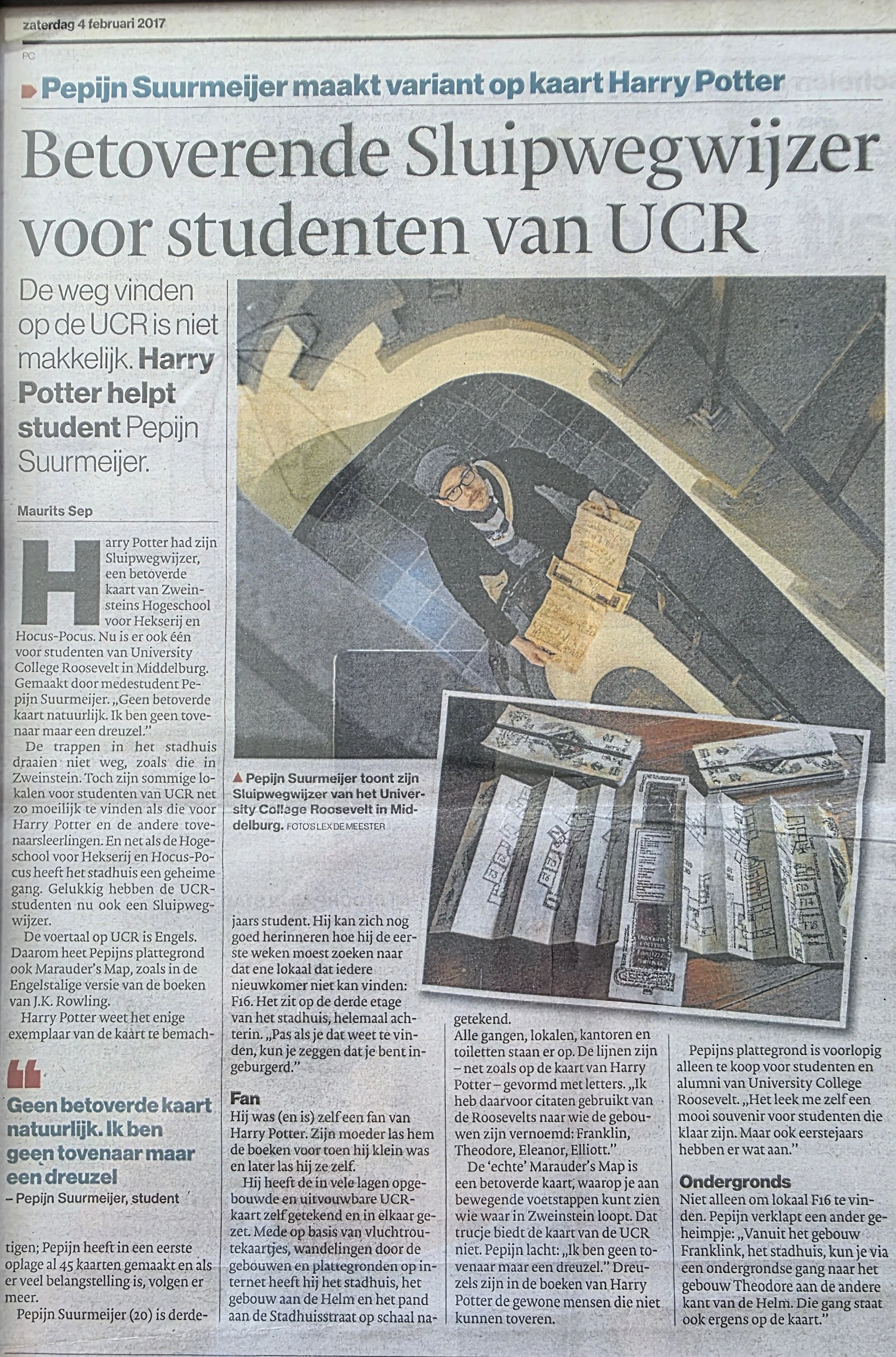 A person dressed in dark clothing and wearing glasses stands on a spiral staircase holding a cardboard box decorated with Harry Potter-themed drawings and symbols. The staircase is in a building with brick walls and a curved yellow railing. The photo is taken from above.