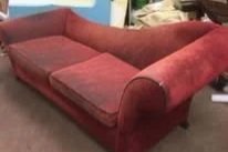 A red velvet sofa with rounded arms in a room.