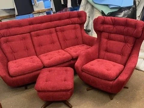 Red upholstered vintage sofa with matching ottoman and a rounded armchair in a furniture store.