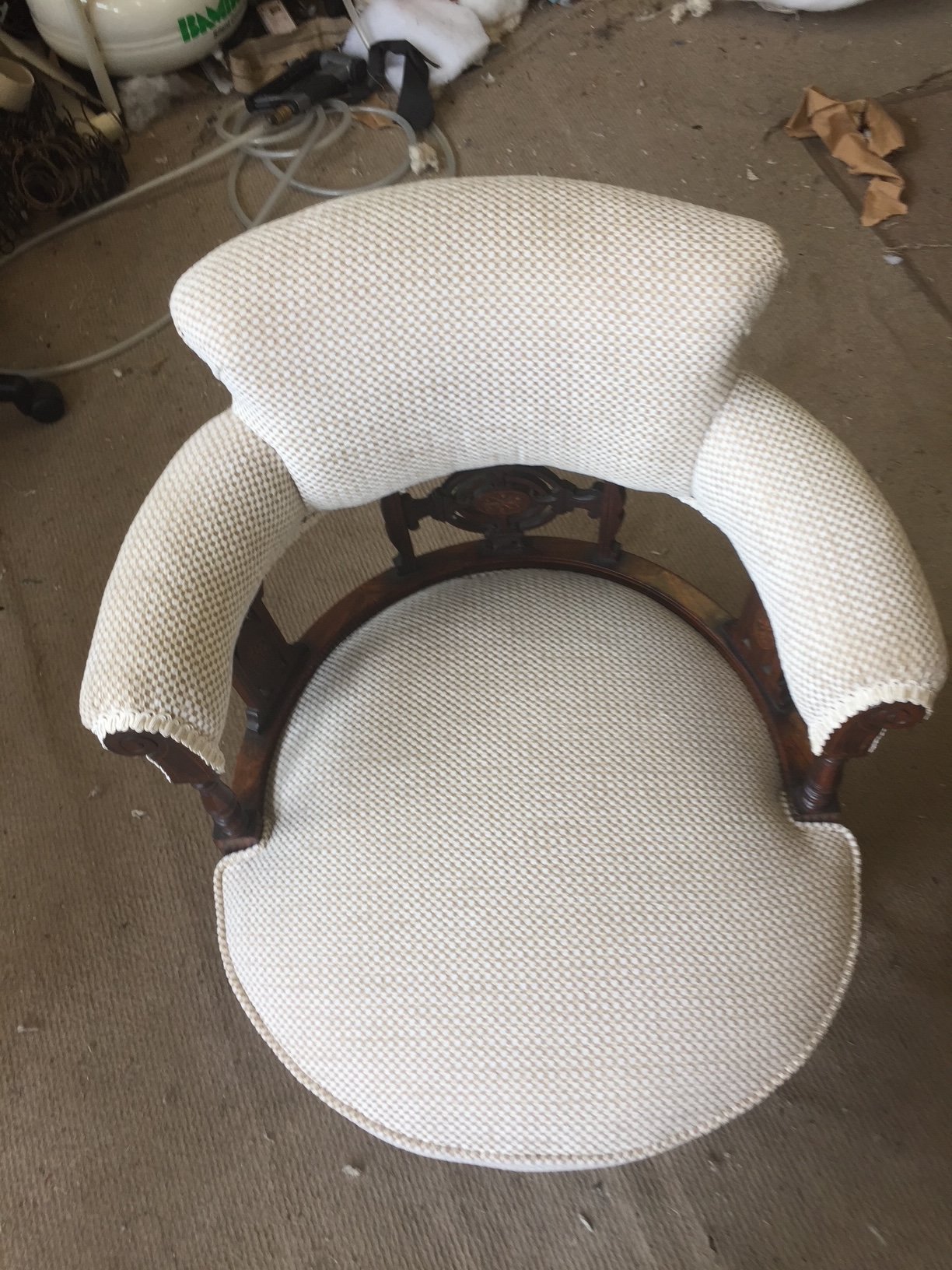 An antique wooden armchair with beige and white patterned upholstery on the backrest and seat, placed on a beige carpeted floor.