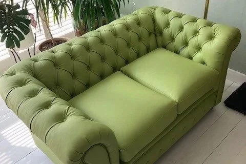 Bright green tufted loveseat with a single seat cushion in a room with plants and light-colored flooring.