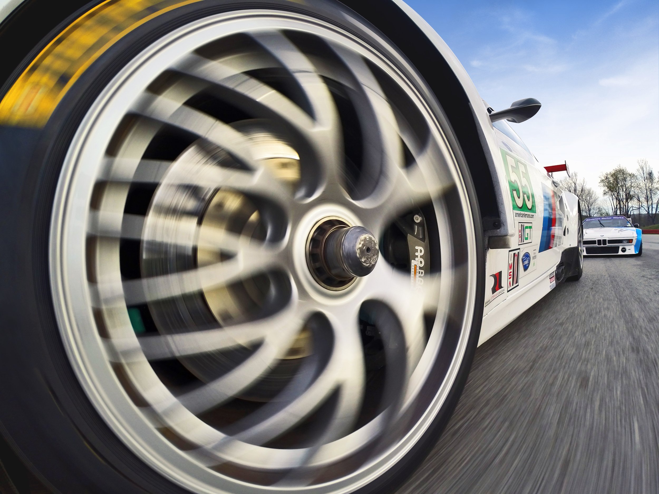 Close-up of a race car tire spinning at high speed, with a blurred background of trees and a clear sky.