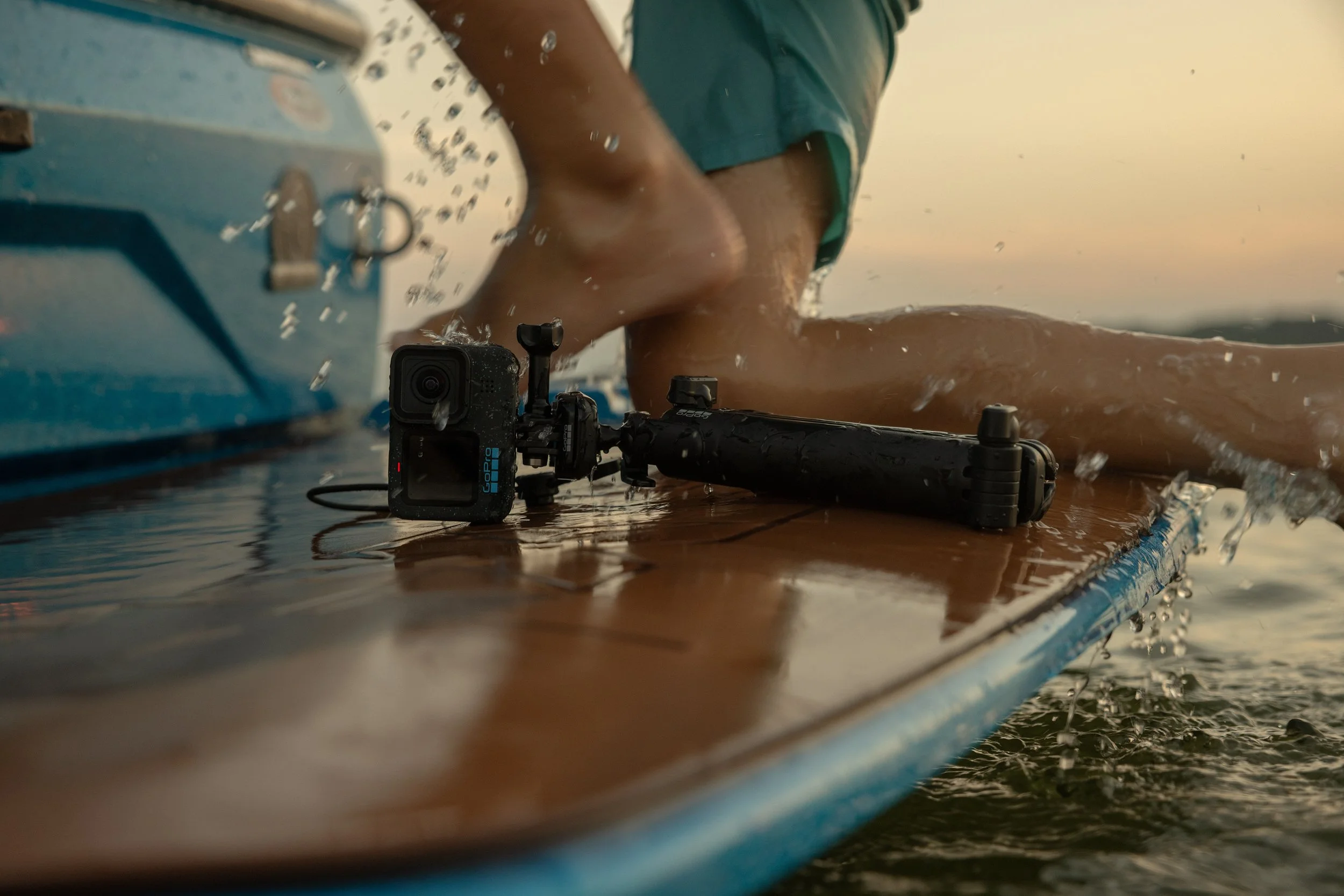 Close-up of a person’s hand operating a drone near water with a camera attached, during sunset or sunrise.
