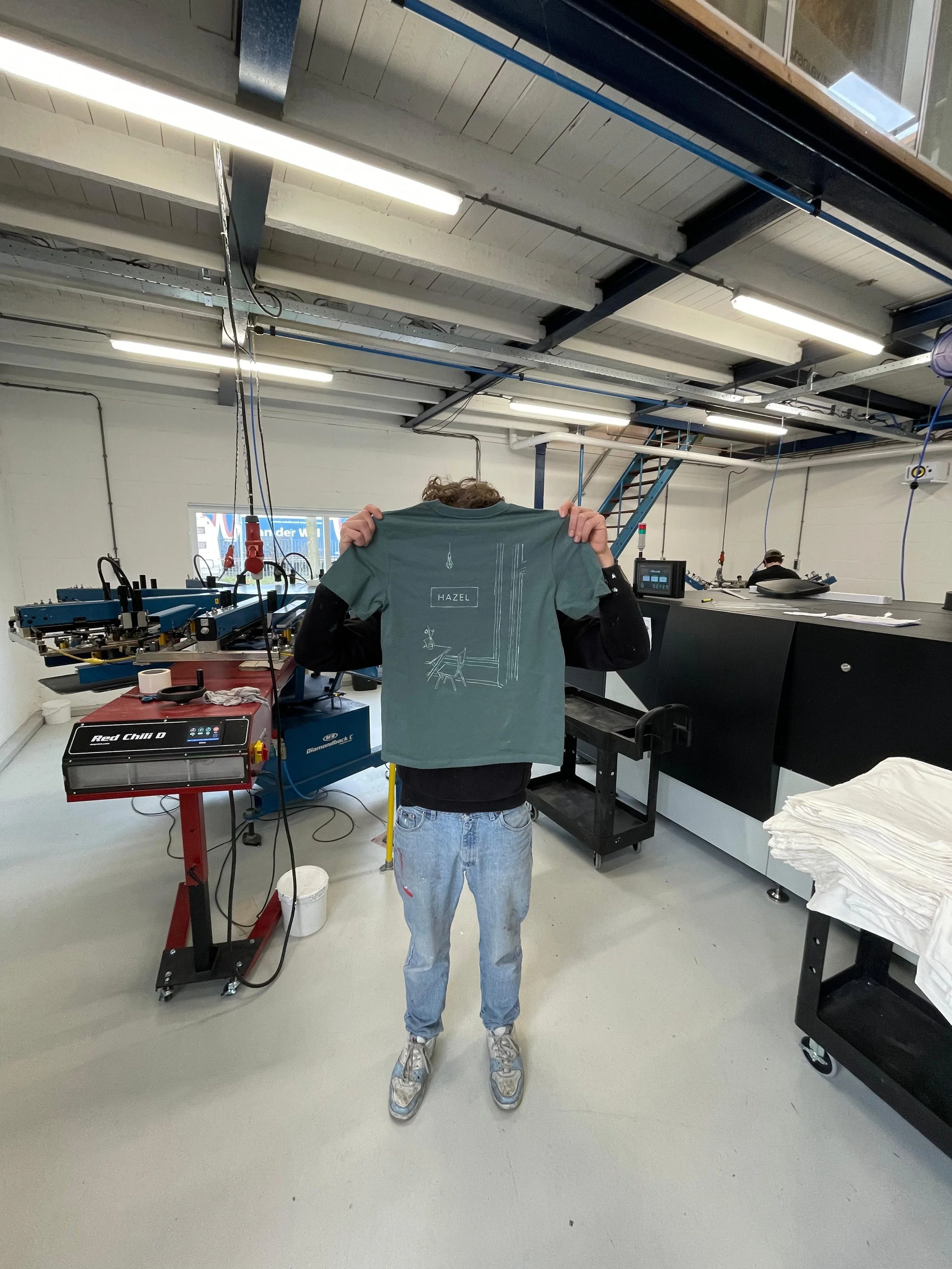 Medewerker toont een bedrukt groen T-shirt in onze professionele textieldrukkerij in Utrecht, gespecialiseerd in duurzame en kwalitatieve textielproductie.