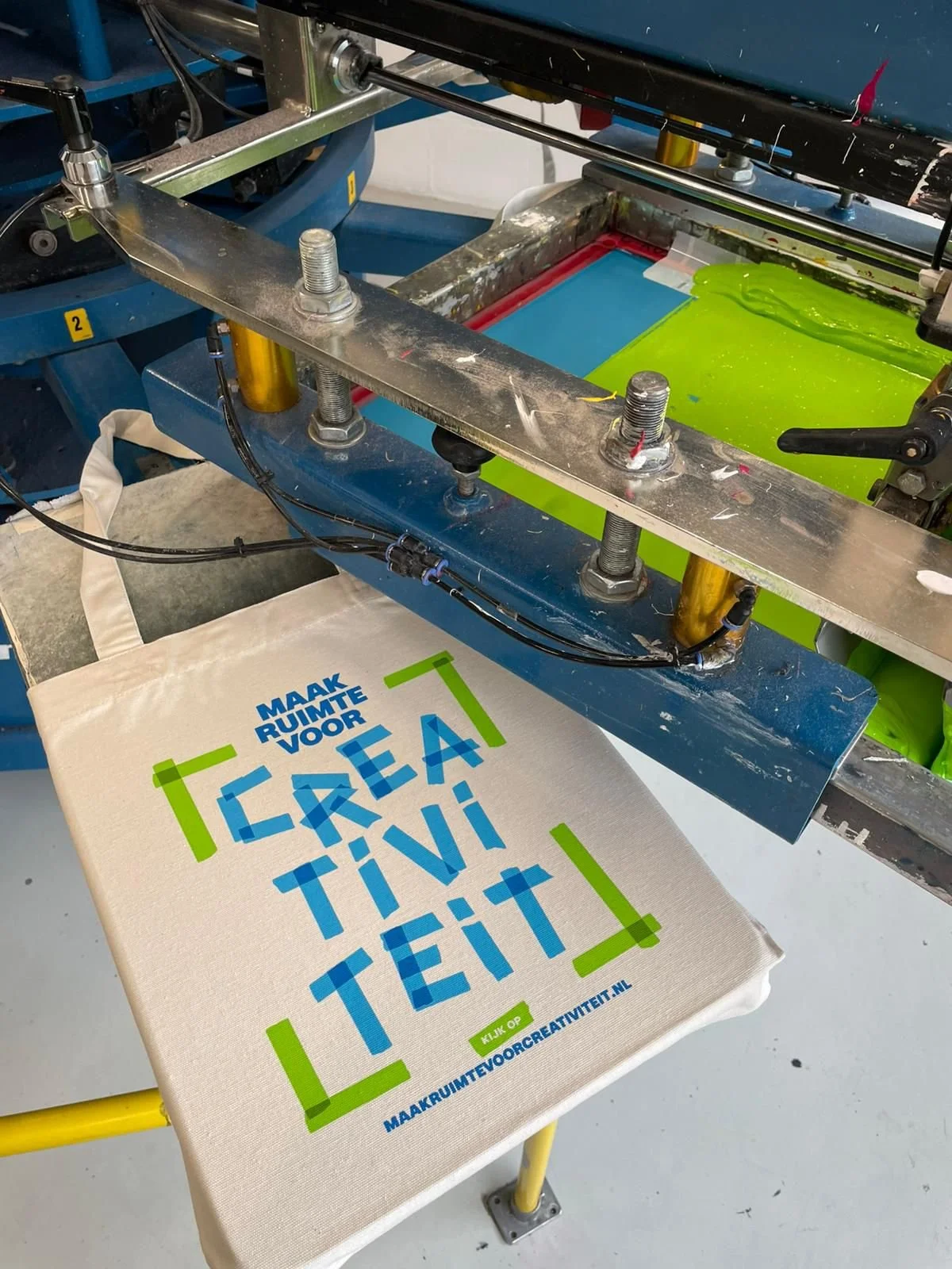 Close-up van een handmatige zeefdrukmachine die inkt op een katoenen tas aanbrengt in onze drukkerij in Utrecht; ambachtelijke kwaliteit voor duurzame textielproductie.