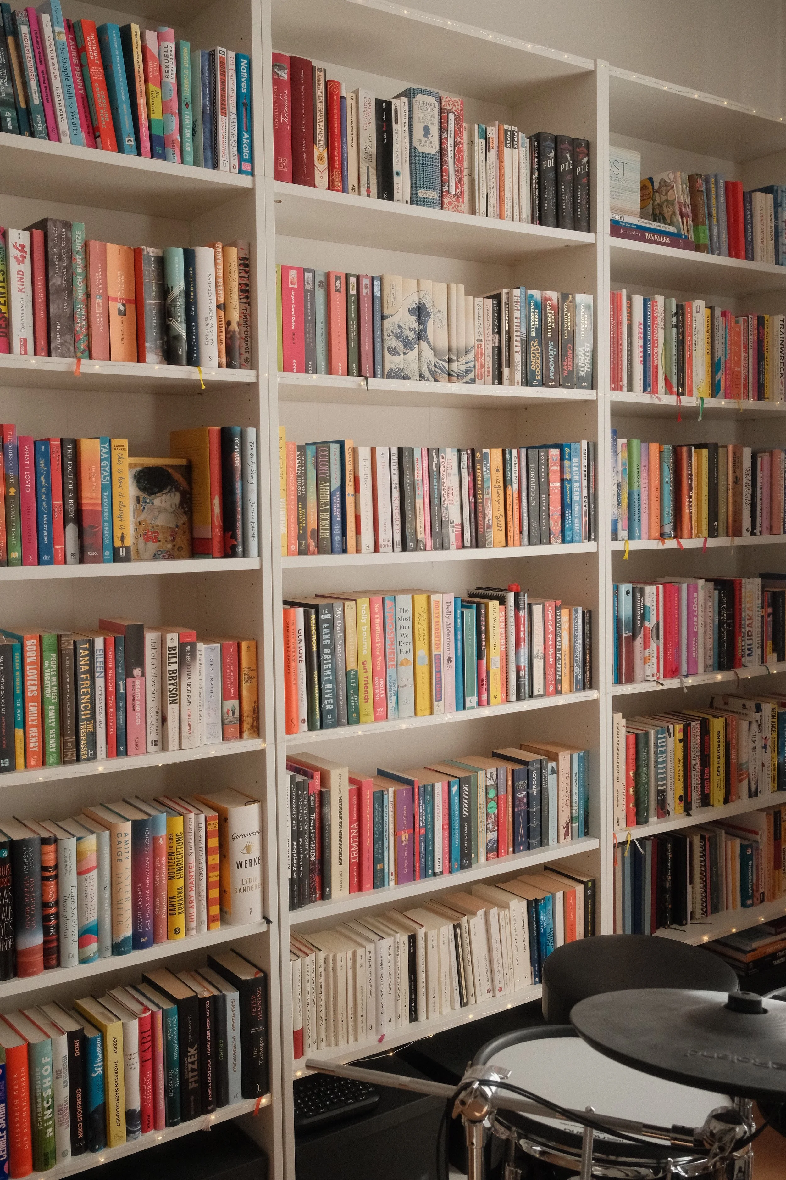 Bücherregale gefüllt mit bunten Büchern in einem Raum, mit einem Drumset im Vordergrund.