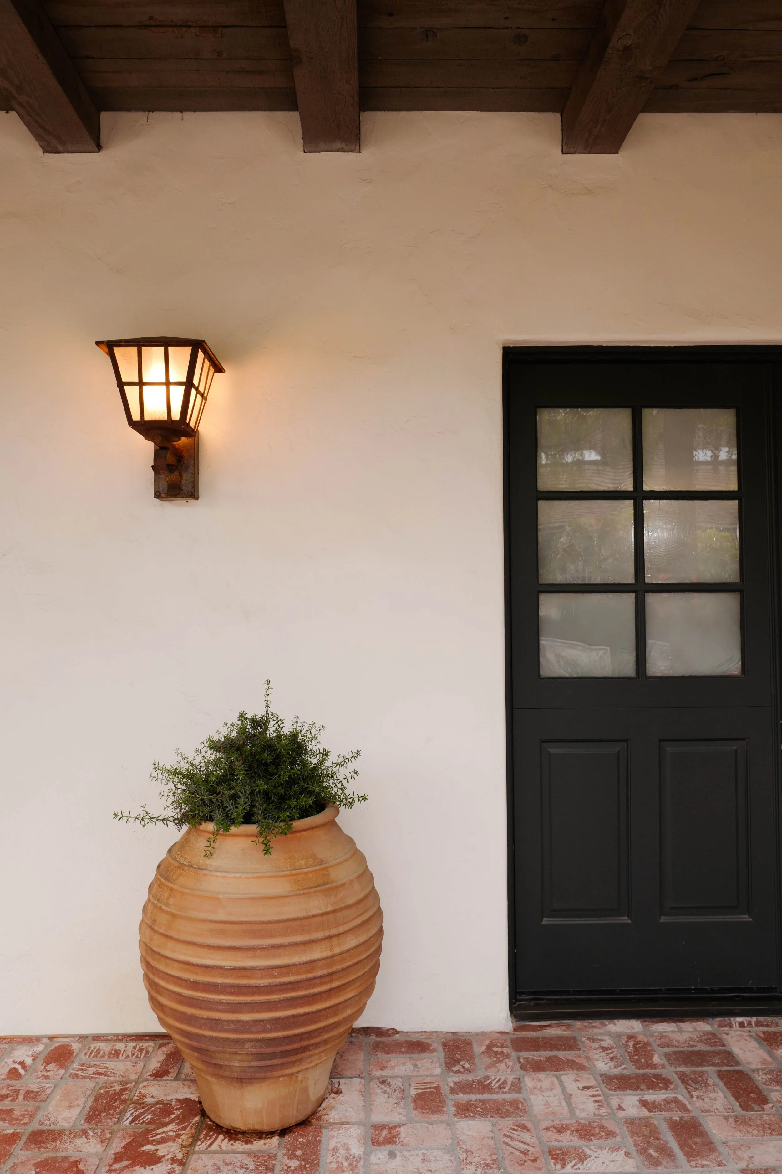 Spanish Revival home entry with terracotta urn, wrought iron wall sconce, and black Dutch door.