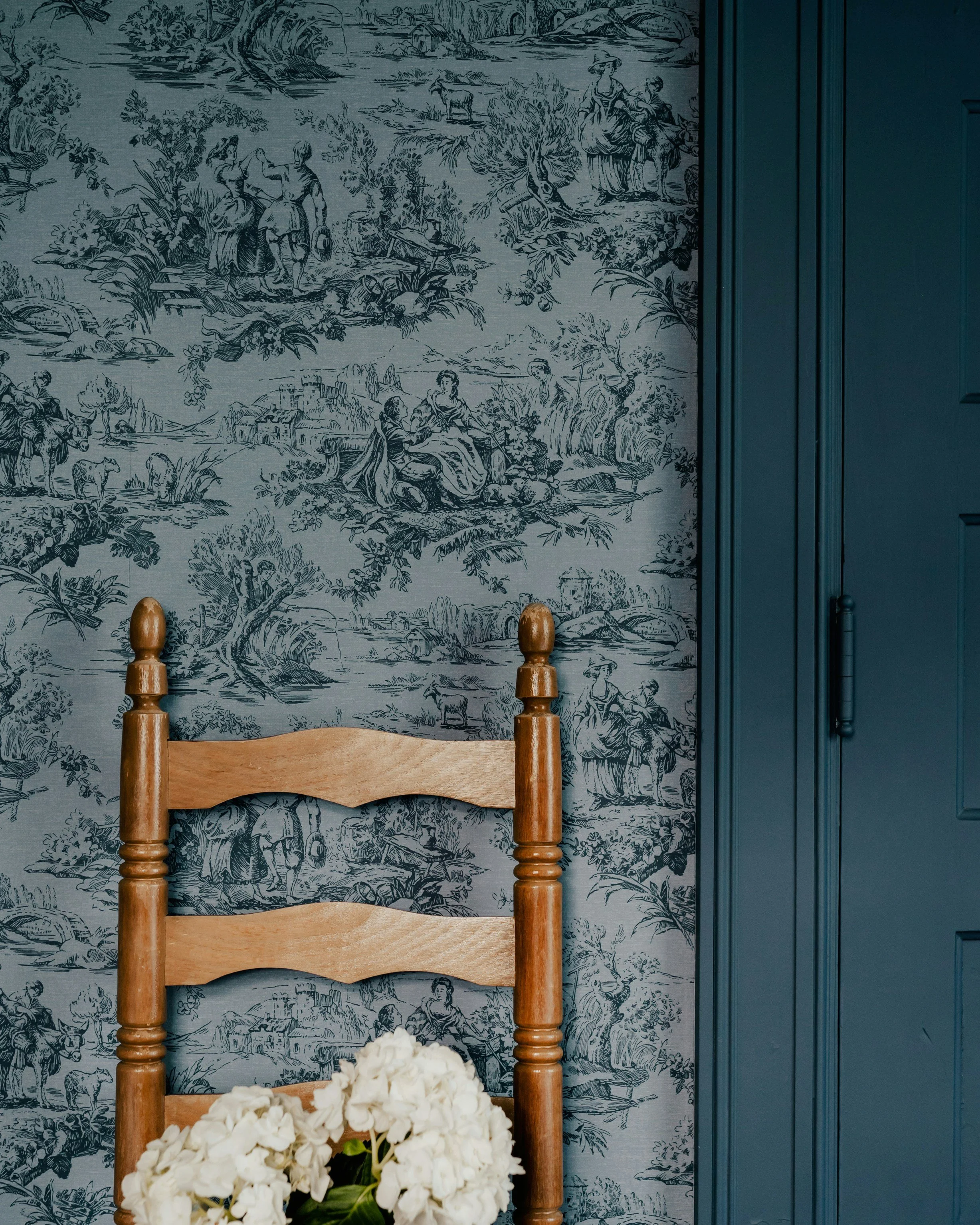 Antique ladder-back chair against blue toile wallpaper with matching painted millwork in a historic interior