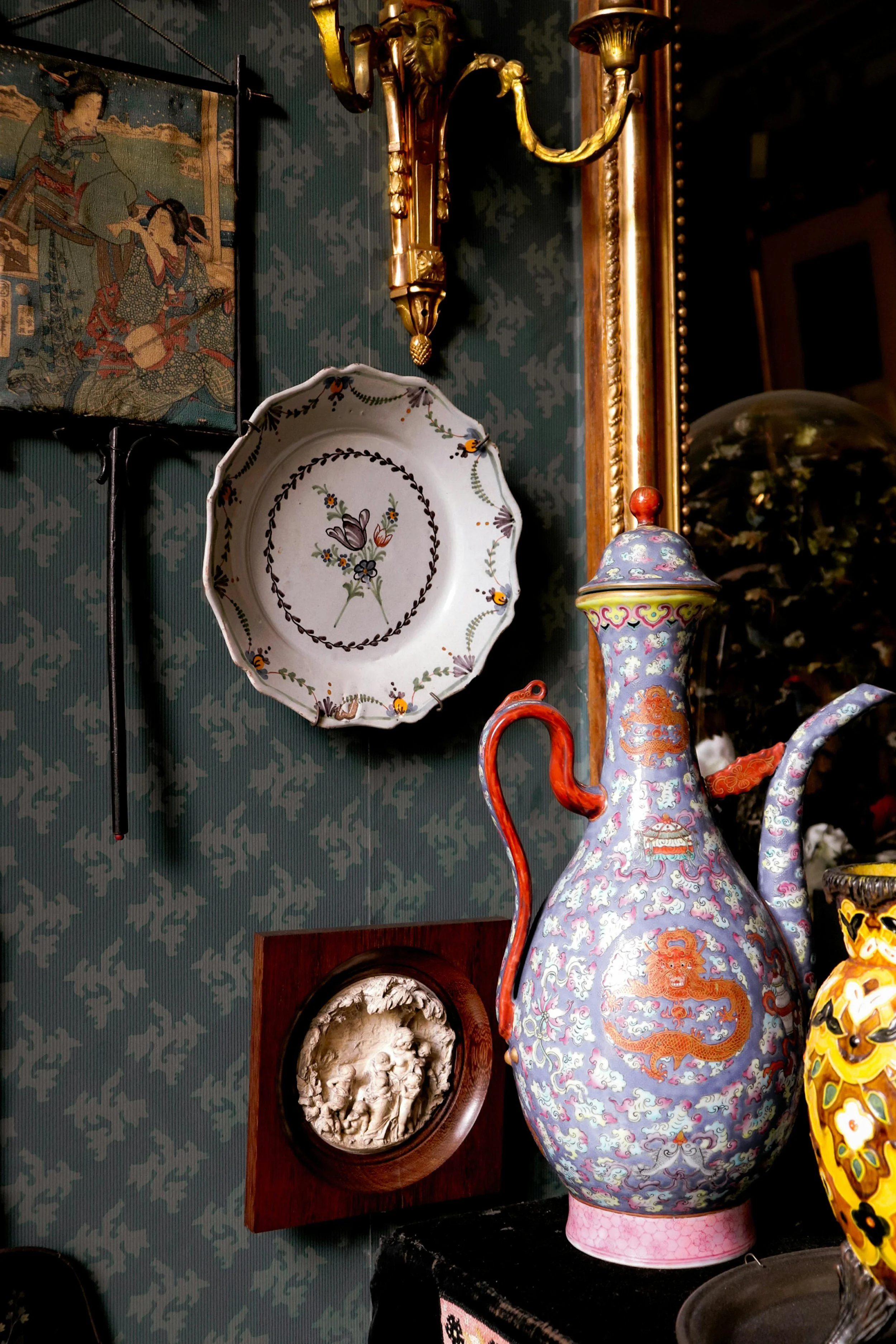 Curated maximalist vignette with hand-painted porcelain vase, decorative plate, and antique wall art