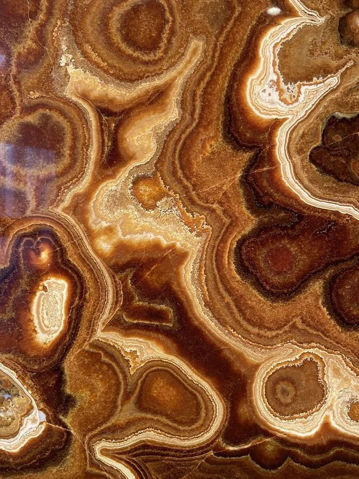 Close-up of a polished brown and tan onyx stone with swirling, layered patterns.