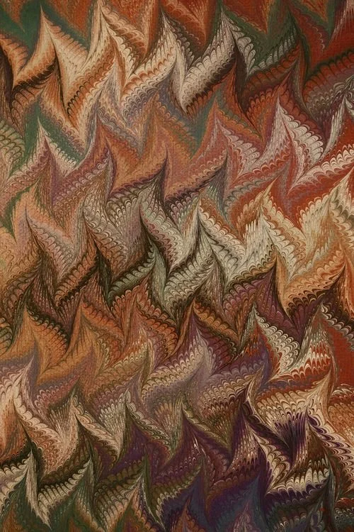 Colorful marbled paper with swirling patterns in shades of brown, orange, green, purple, and white.