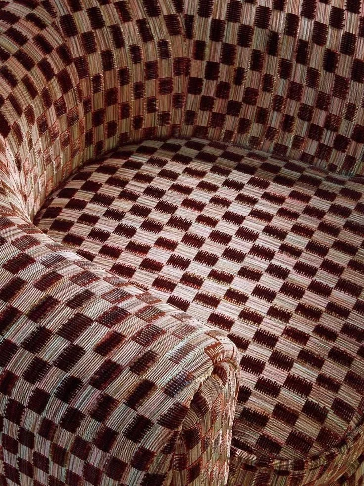 Close-up of a patterned armchair with a checkered upholstery in shades of brown, beige, and red.