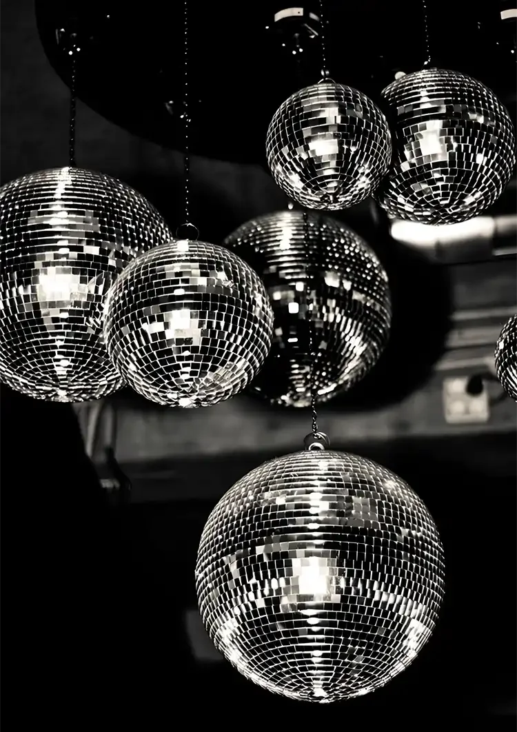 Mehrere Disco-Kugeln hängen von der Decke, reflektieren Licht, in Schwarz-Weiß-Fotografie.