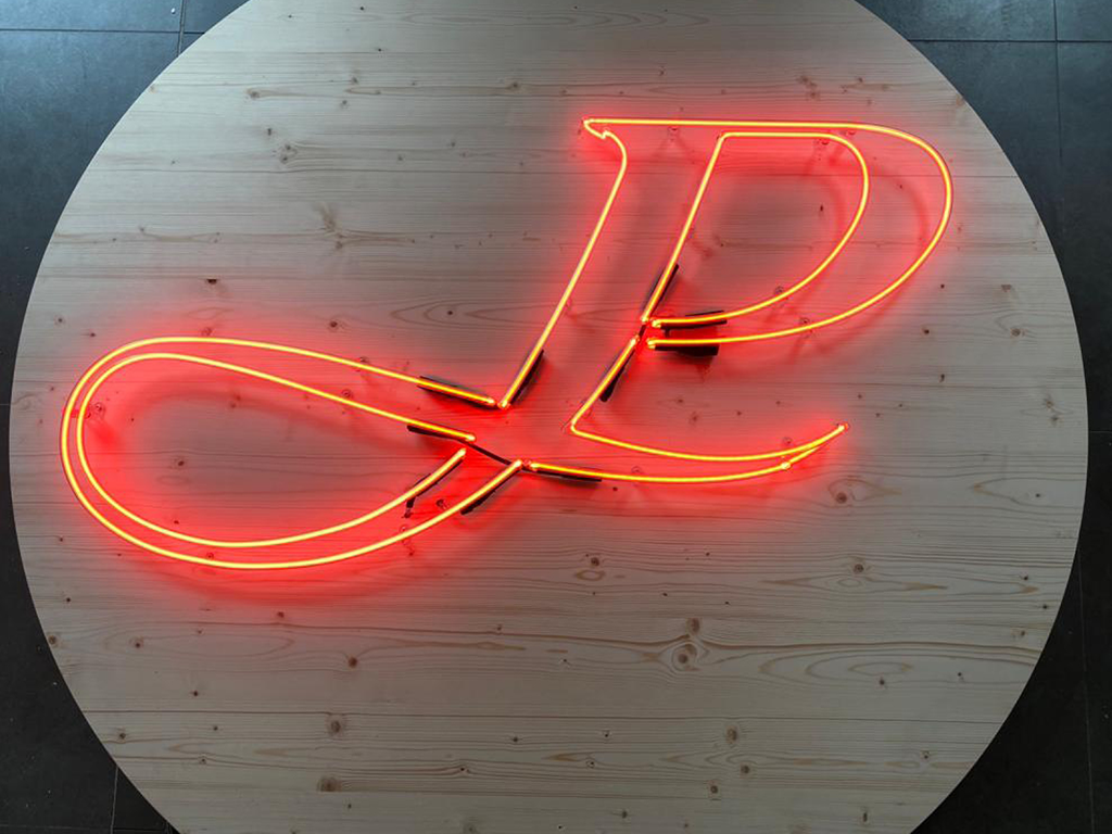 Neon-Leuchtschild mit den Buchstaben 'JP' in rot, auf rundem Holztablett