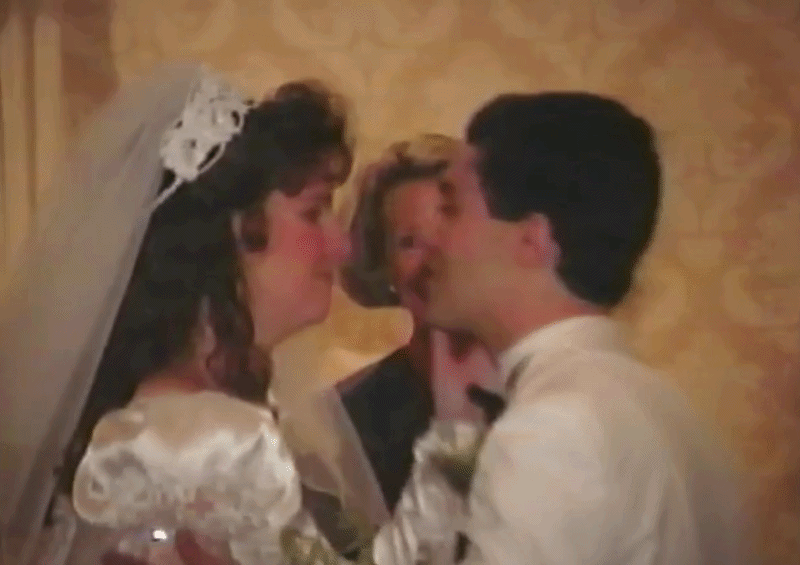 A bride and groom sharing a kiss during their wedding ceremony, with an officiant standing behind them.