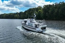 A white boat cruising on a river surrounded by green trees under a partly cloudy sky.