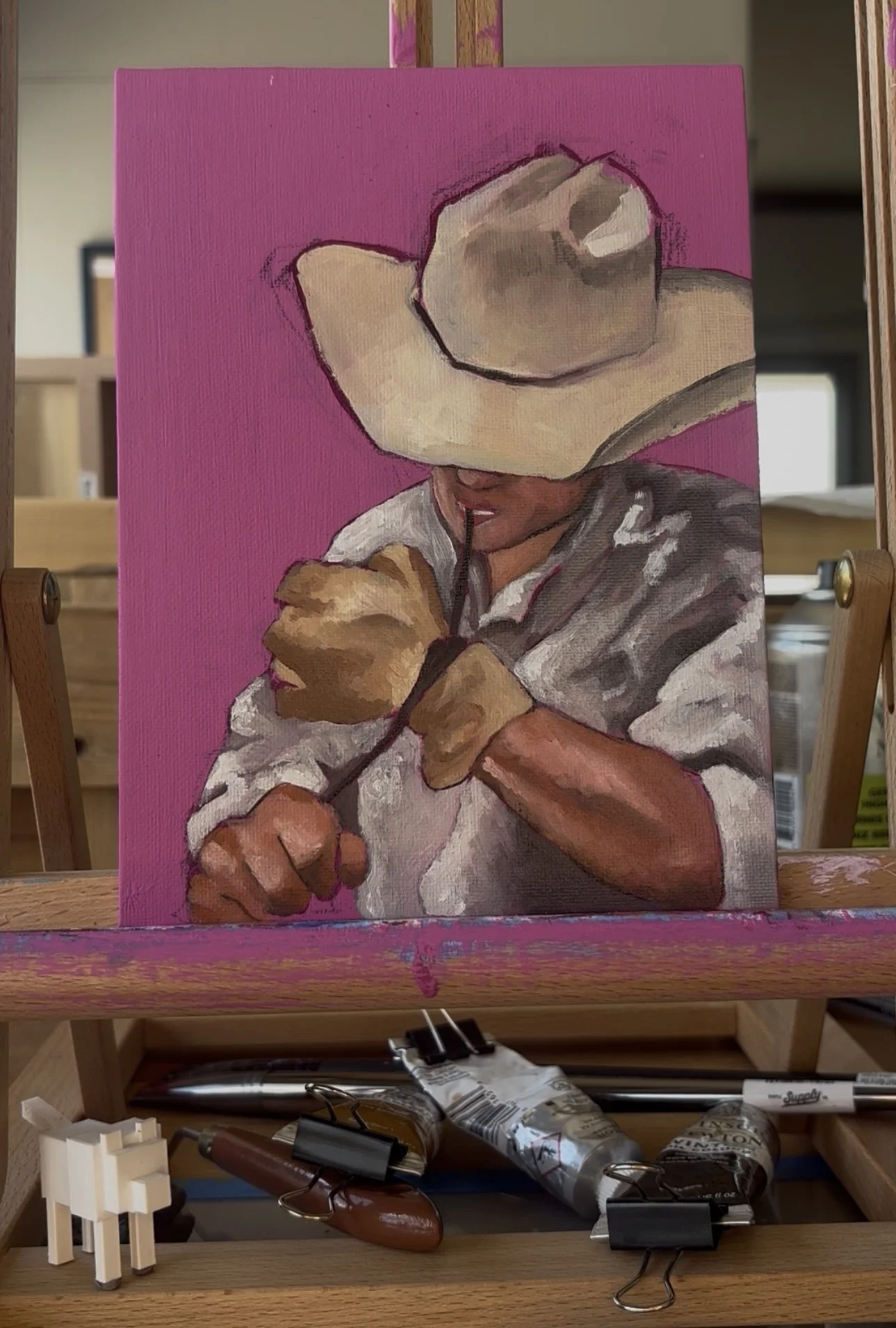 A painting of a person with a large beige cowboy hat, wearing a gray and white shirt, with their head down and hand near their mouth, set against a bright pink background.